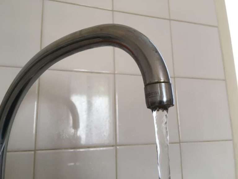 Tap with water running against a tiled background